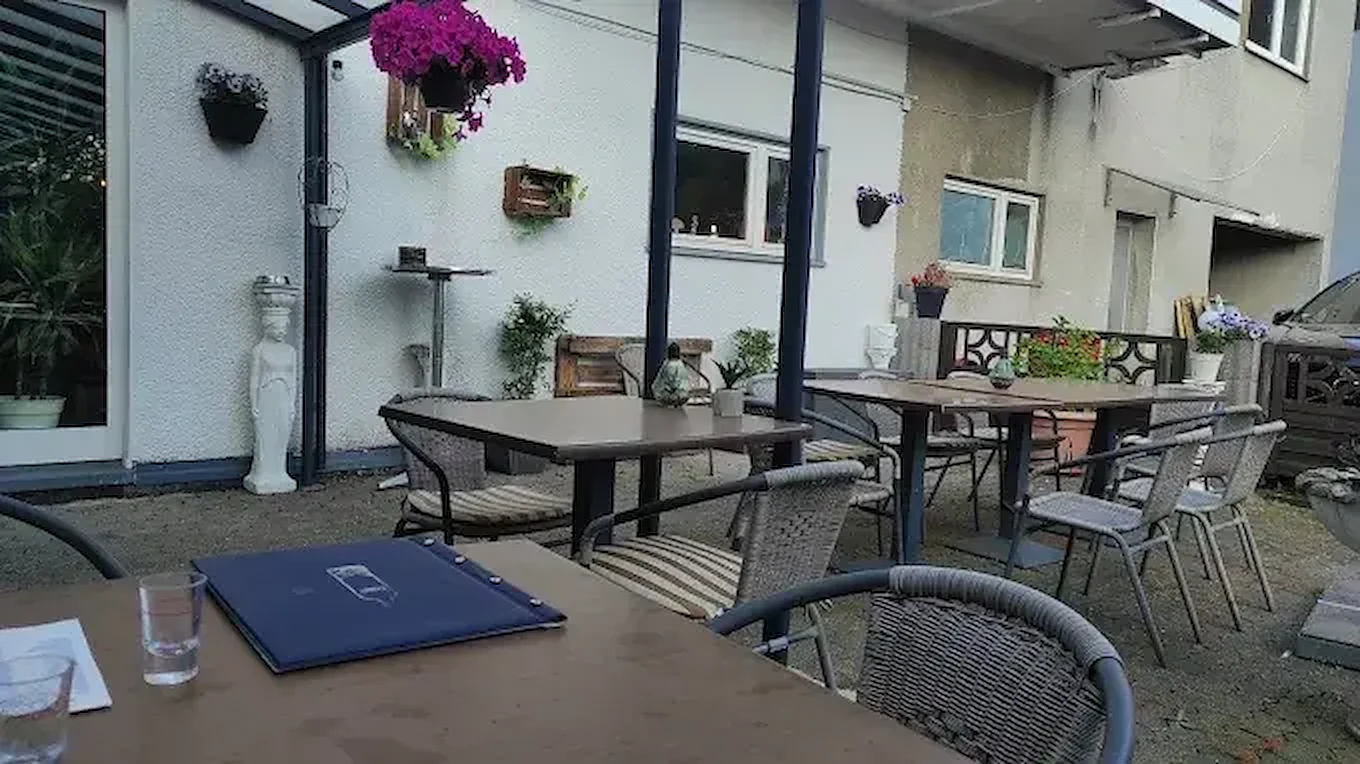 Außenbereich mit Tischen, Stühlen, Blumentöpfen und einer großen weißen Skulptur